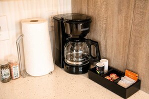 Eine Küchenzeile mit Kaffeemaschine, Küchenpapierrolle und einer Gewürzregal mit Gläsern.