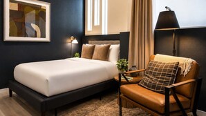 Quarto de hotel com uma cama, uma cadeira, um abajur e um quadro na parede.