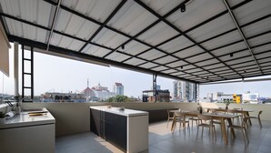 A rooftop terrace with a kitchen area, dining space, and a view of the city skyline.