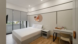 A modern bedroom with a bed, bedside table, desk, chair, and a large window.