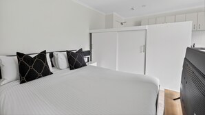 Habitación de hotel con cama, paredes blancas, armario y kitchenette.