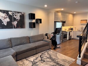A modern living room with a grey sofa, a world map on the wall, and a kitchen in the background. - 3 Bedroom Townhouse with Outdoor Rooftop Deck (Seattle)