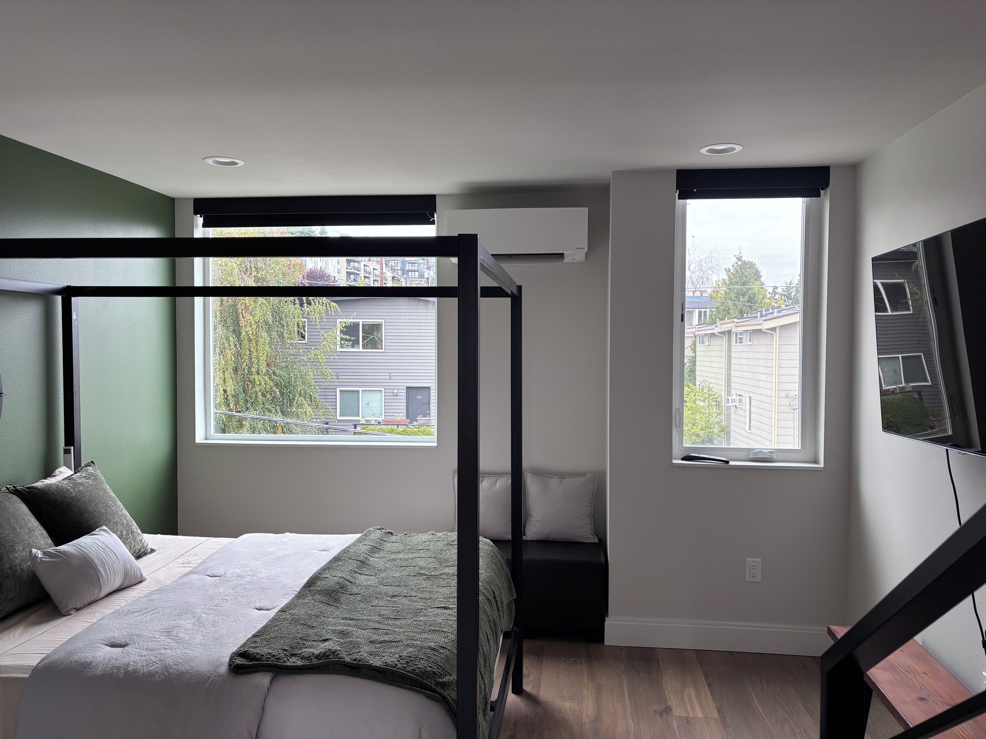 A bedroom with a four-poster bed, a large window, and a view of a residential building.