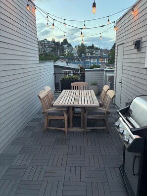 A patio with a wooden table and chairs, a grill, and string lights. - 3 Bedroom Townhouse with Outdoor Rooftop Deck (Seattle)