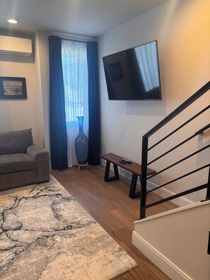 A living room with a sofa, a coffee table, a TV mounted on the wall, a staircase, and a large window with curtains. - 3 Bedroom Townhouse with Outdoor Rooftop Deck (Seattle)