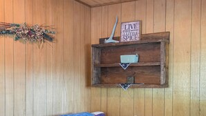 A wooden-paneled room with a bed, a shelf with a sign, and a light fixture.