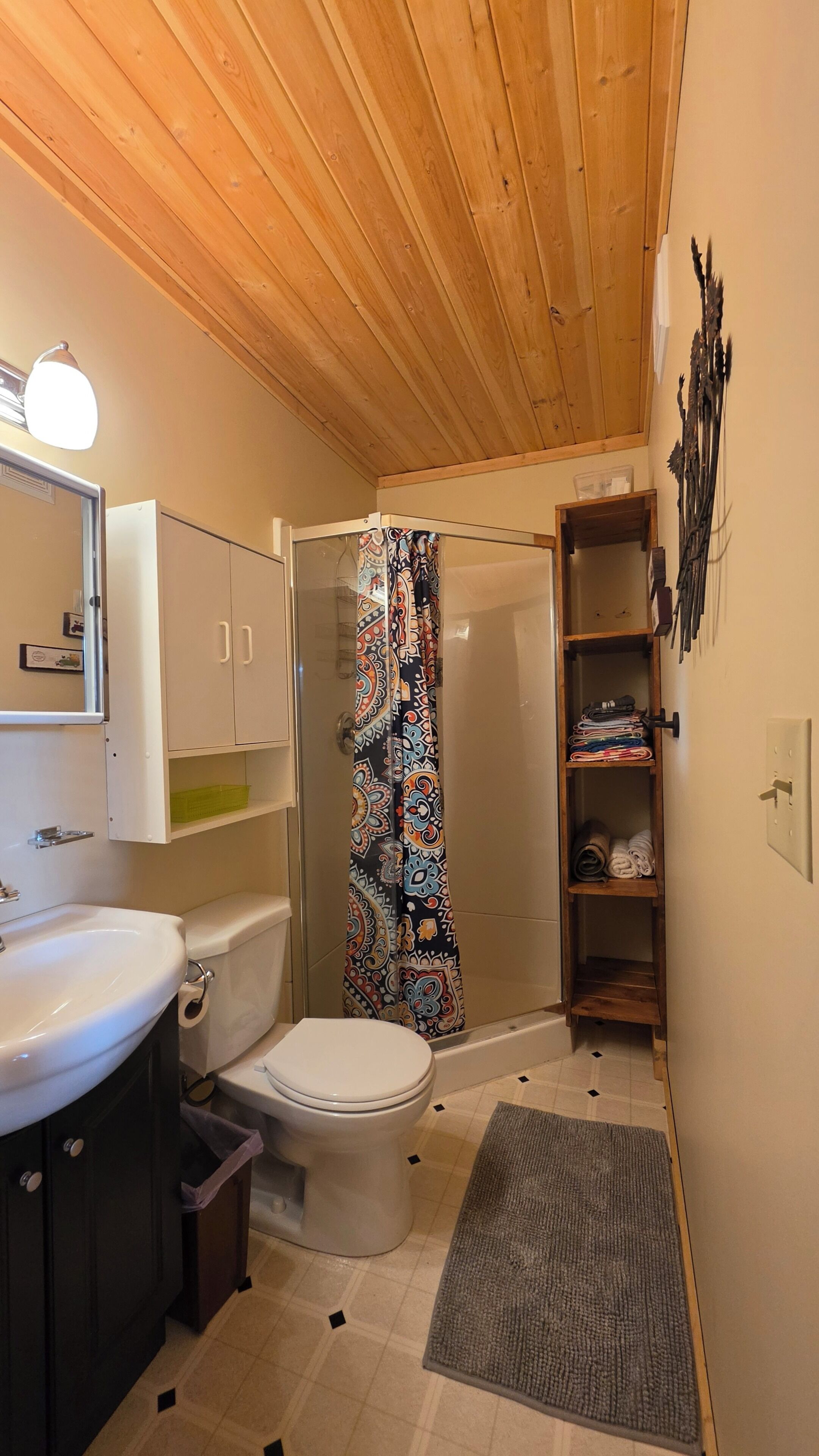 A compact bathroom with a toilet, sink, shower, and a wooden ceiling.