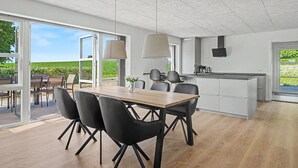 Une cuisine moderne dotée d’un grand îlot central, d’un coin repas avec une table en bois et des chaises noires, et offrant une vue sur un vignoble grâce à de grandes portes vitrées.