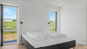 Une chambre à coucher avec un lit, deux fenêtres et une vue sur un champ.
