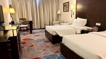 A hotel room with two beds, a desk, a chair, a TV, and a patterned carpet.