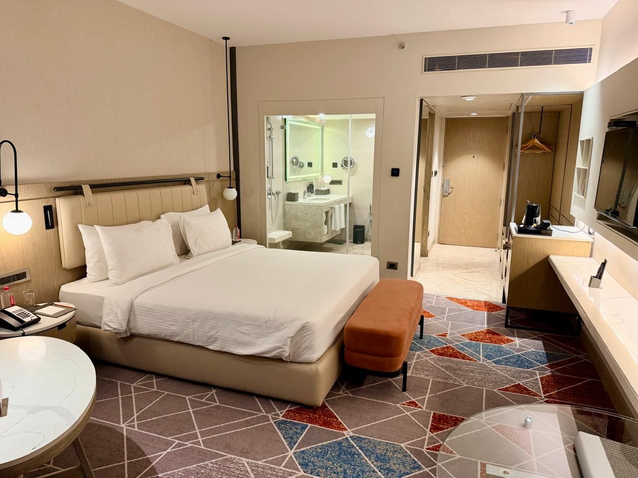 Una camera d'albergo con un letto, un comodino e un bagno visibile attraverso una porta aperta.