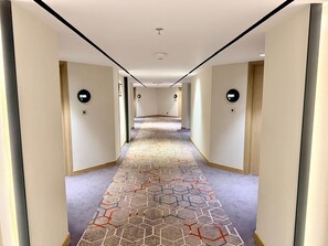 A hotel hallway with a patterned carpet, doors with light switches, and a ceiling light fixture. - J J Plaza JHV Cantonment Varanasi (Varanasi)