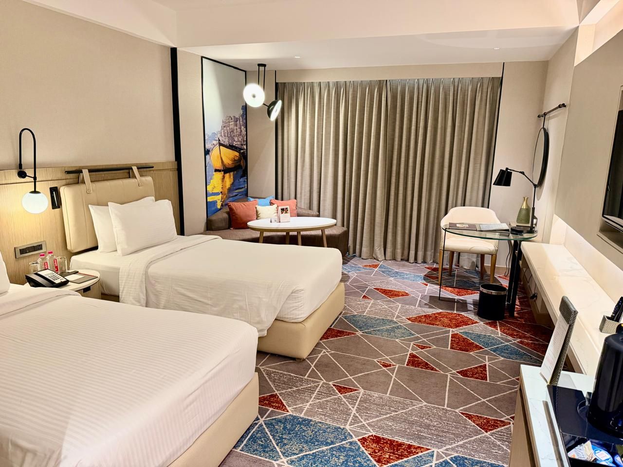 A hotel room with two beds, a small table, a chair, a desk, and a television.