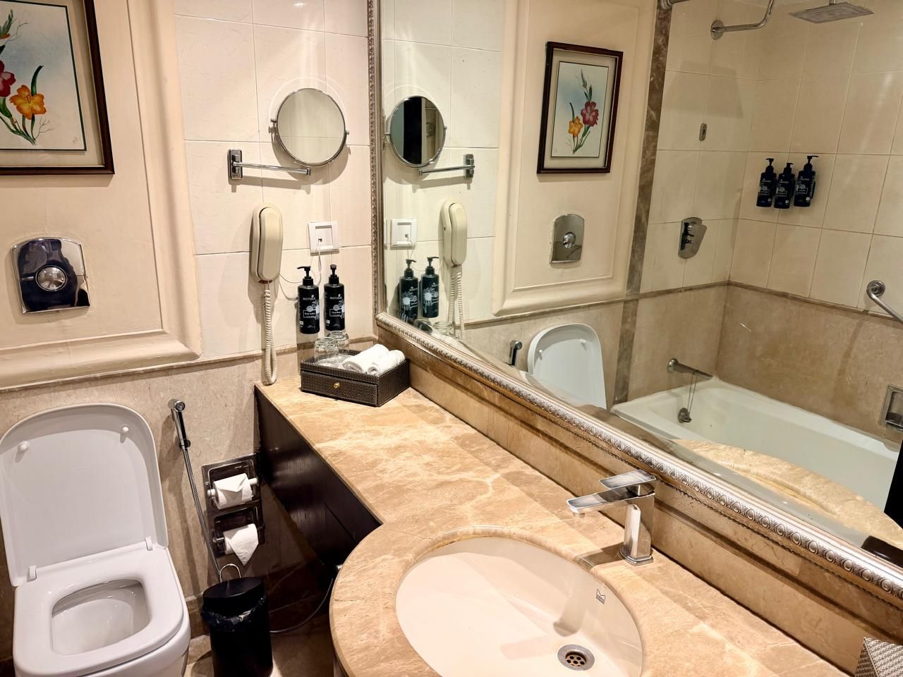 Un baño con inodoro, lavamanos y bañera. Hay espejos, un perchero para toallas y artículos de aseo.