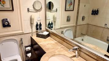 Un baño con inodoro, lavamanos y bañera. Hay espejos, un perchero para toallas y artículos de aseo.