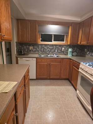 A kitchen with wooden cabinets, a stainless steel sink, a dishwasher, a stove, and a window above the sink. - Adorable 2-bedroom house with AC in Kenosha perfect for relaxing, (Kenosha)