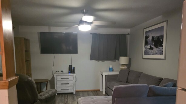 En stue med sofa, fjernsyn, lampe og et billede i ramme på væggen.