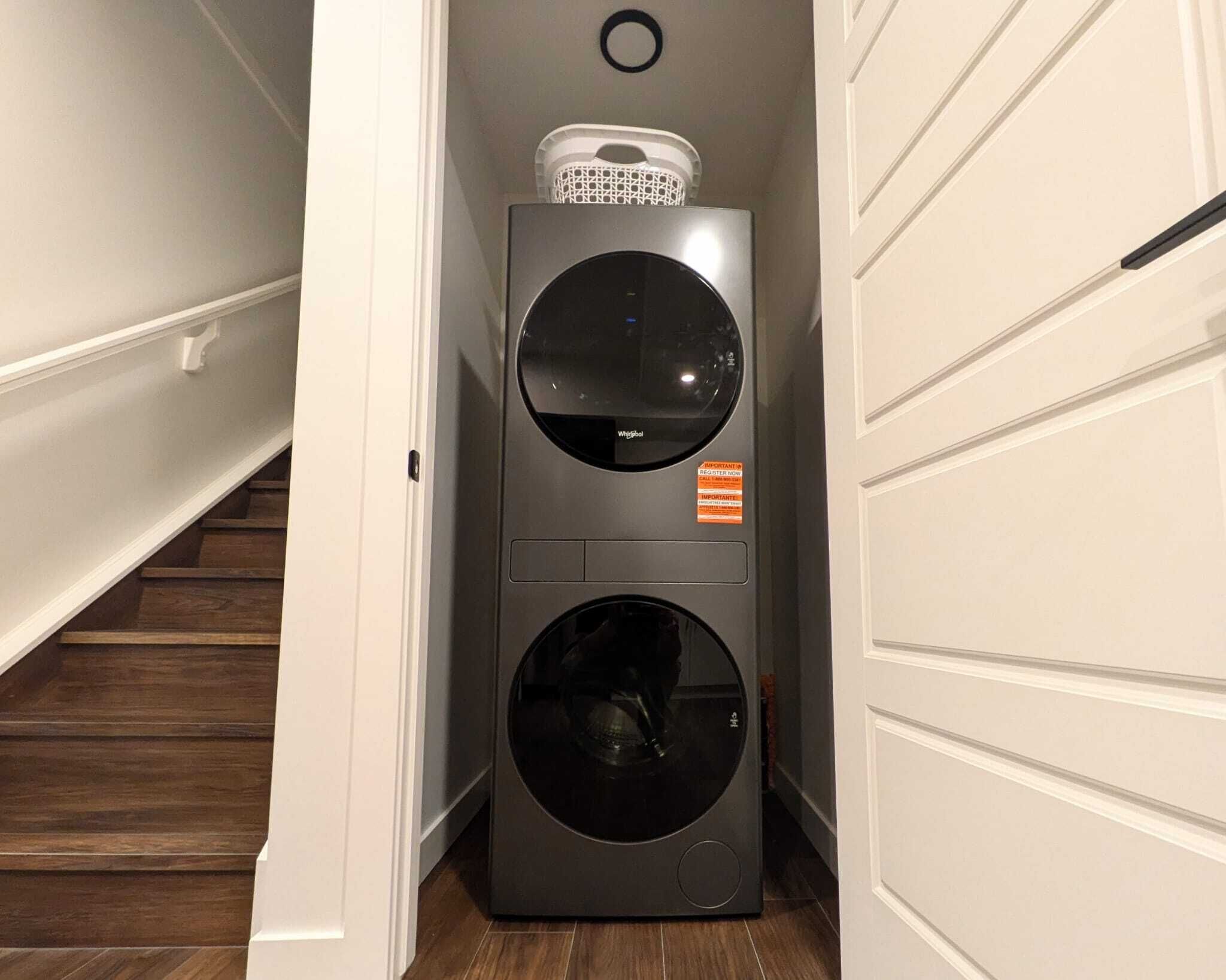 A compact, modern washer and dryer unit in a narrow hallway with wooden flooring and white walls.