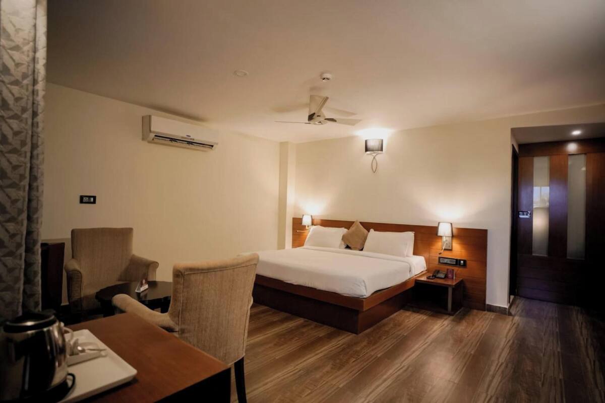 Een hotelkamer met een bed, twee nachtkastjes, een stoel, een bureau, een airconditioning en een plafondventilator.
