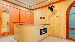A hotel reception area with a curved counter, a large mirror, and a fan on the wall.