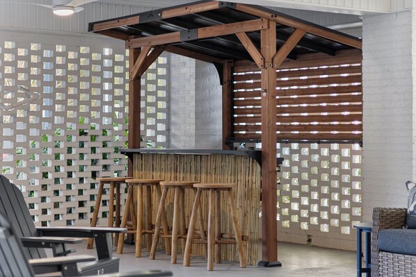 A bar area with wooden stools and a counter, surrounded by a lattice fence and a white brick wall.