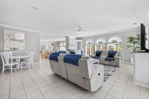 A spacious living area with a sofa set, a dining table with chairs, and a kitchen area in the background.