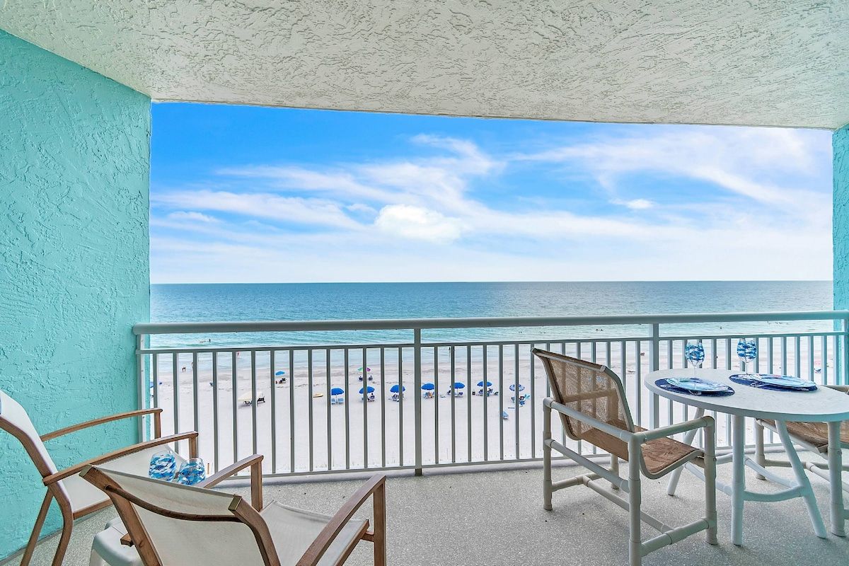 A balcony with a view of the beach, equipped with chairs and a table.