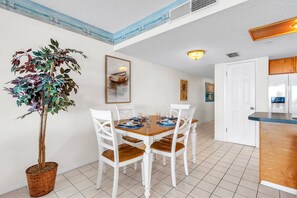 A dining area with a table set for four, white chairs, a potted plant, and artwork on the walls. - Top Floor Beachfront with Amazing Views! Heated Pool, Free Parking, Free Activities! ~ 506 Chateaux (Indian Shores)