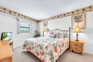 A bedroom with a bed, bedside tables, a desk, a television, and a window with blinds. - Top Floor Beachfront with Amazing Views! Heated Pool, Free Parking, Free Activities! ~ 506 Chateaux (Indian Shores)