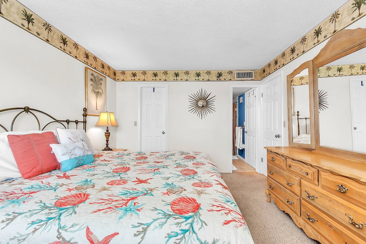 A bedroom with a bed, dresser, and a door leading to another room.