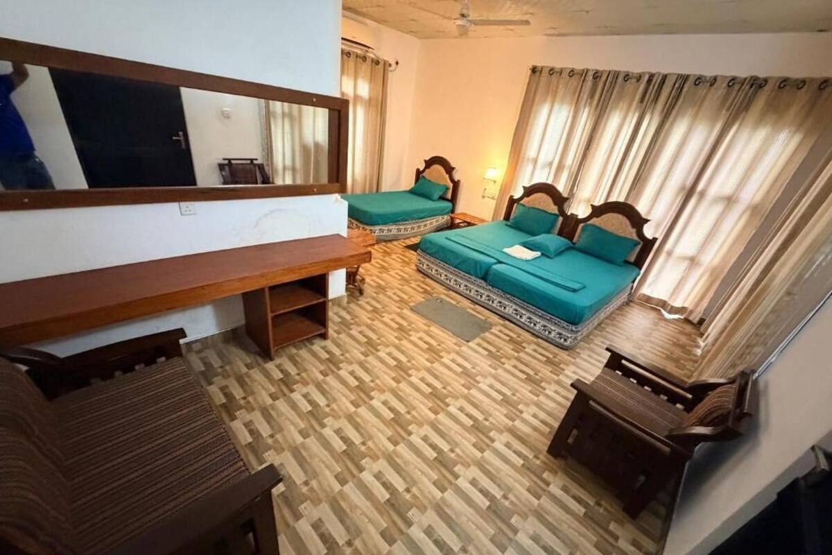 Quarto com duas camas, um banco de madeira, uma pequena mesa e um espelho na parede.