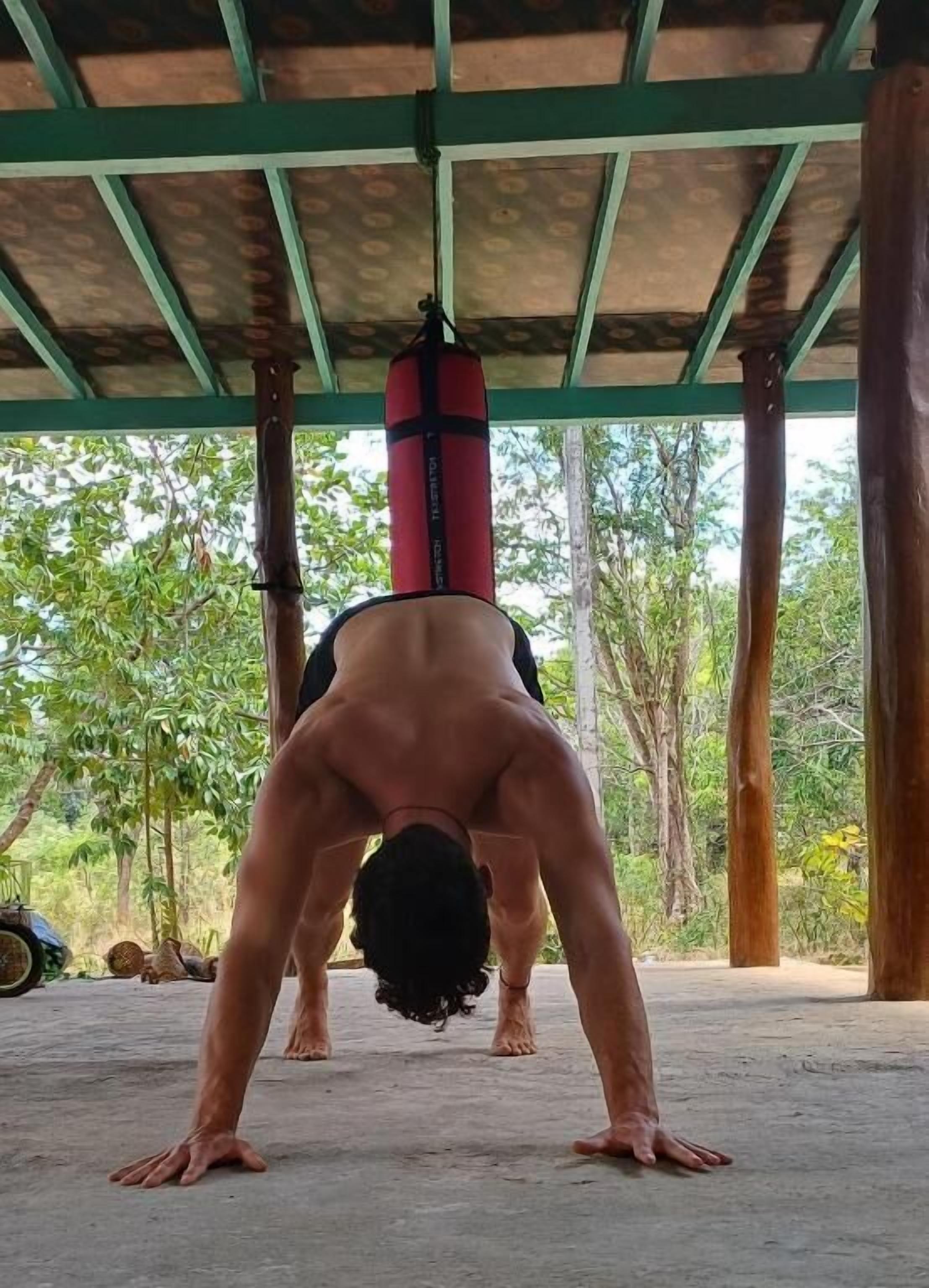A person performing a handstand under a covered area with a red punching bag.
