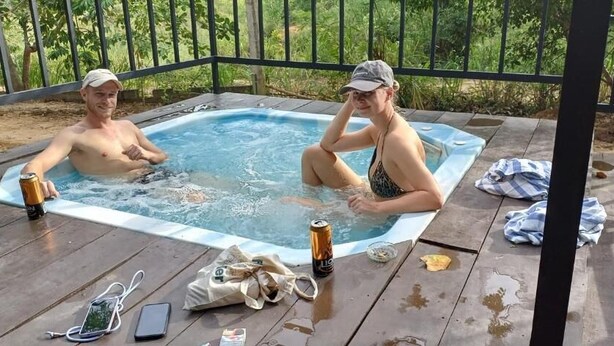 A hot tub with two people, a wooden deck, and a metal railing.