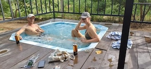 A hot tub with two people, a wooden deck, and a metal railing.