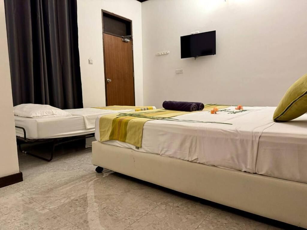 A room with two beds, a flat-screen TV, a wooden door, and a curtain.