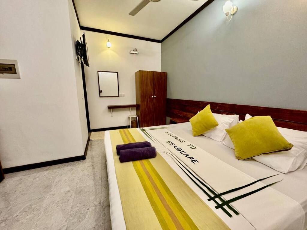 A hotel room with a bed, a wooden wardrobe, a nightstand, and a wall-mounted light fixture.