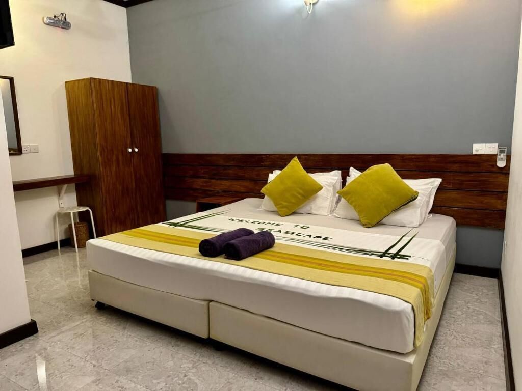 A neatly made bed with a welcome mat, a wooden wardrobe, and a small table.