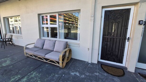 Quarto com sofá, porta com grade de metal e janela com vista para um edifício.