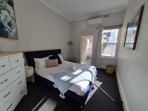 Ein Schlafzimmer mit Bett, Kommode und einem Fenster mit Vorhängen.