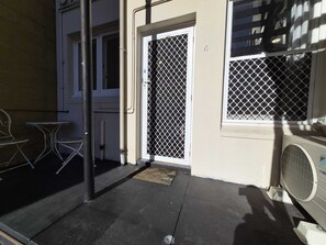 A building entrance with a metal gate, a small outdoor seating area with metal tables and chairs, and a window with a metal grill. - Comfortable Apartment in Fremantle (Fremantle)