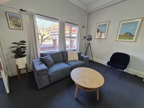 A living room with a grey sofa, a round wooden coffee table, a potted plant, a tripod, and two framed pictures on the wall. - Comfortable Apartment in Fremantle (Fremantle)