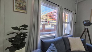 Quarto com sofá, planta em vaso, quadro e janela com vista para um edifício.