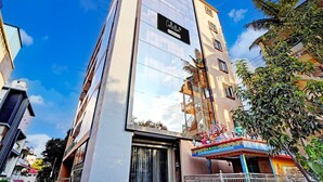 A modern hotel with a reflective glass facade, a prominent 'Collection' sign, and a traditional decorative structure with statues. - Saver Single Bangalore Inn (Bengaluru)