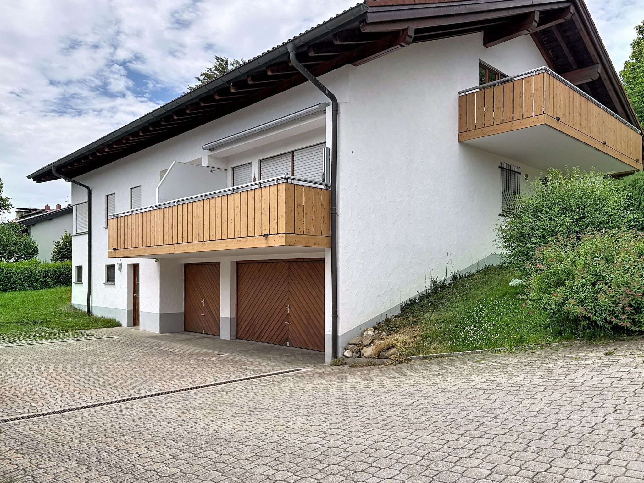 A modern two-story house with a balcony, garage doors, and a paved driveway.