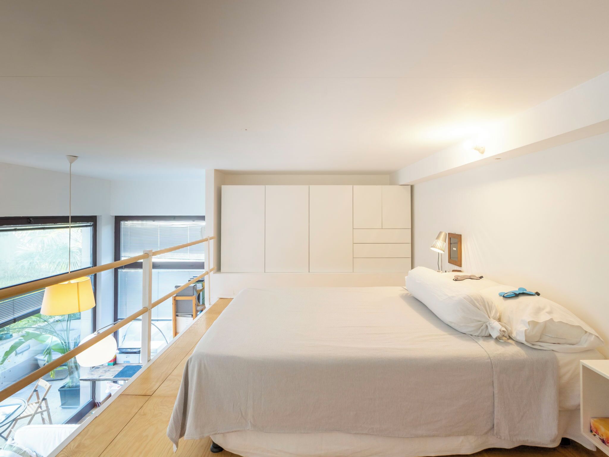 A modern bedroom with a large bed, a bedside table, a lamp, and a view of the outdoors.