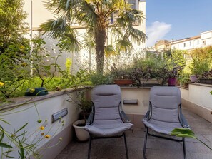 Un balcón con dos sillas, plantas en macetas y una palmera.