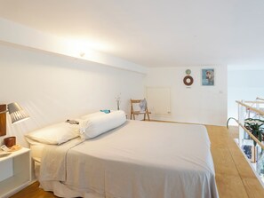 A bedroom with a bed, bedside table, lamp, chair, fan, and a wall with a door and two circular decorations. - NoLo Garden Loft by Interhome (Milan)