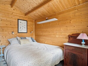 A wooden-paneled room with a bed, a nightstand, a lamp, and a framed picture on the wall.
