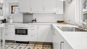 Une cuisine moderne avec des meubles blancs, un four encastré, un évier et une fenêtre.