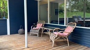 Une terrasse en bois, meublée de meubles en osier, et une porte vitrée donnant sur un espace abrité.